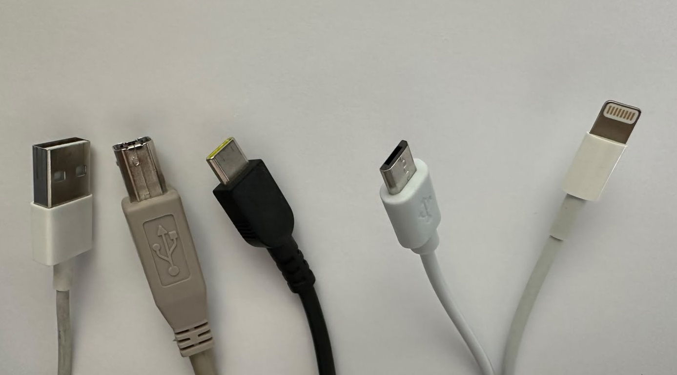 A variety of USB cables and charging showing different standards: USB-A, USB-B, USB-C, micro-USB, and flash cable